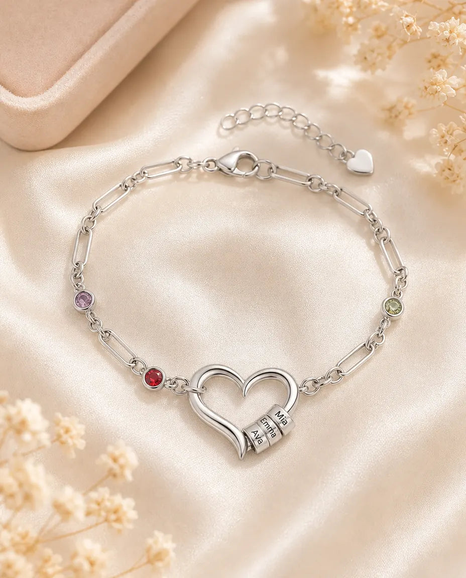 Personalisiertes Silberarmband mit offenem Herz, Namensperlen und Geburtssteinen auf cremefarbener Seide